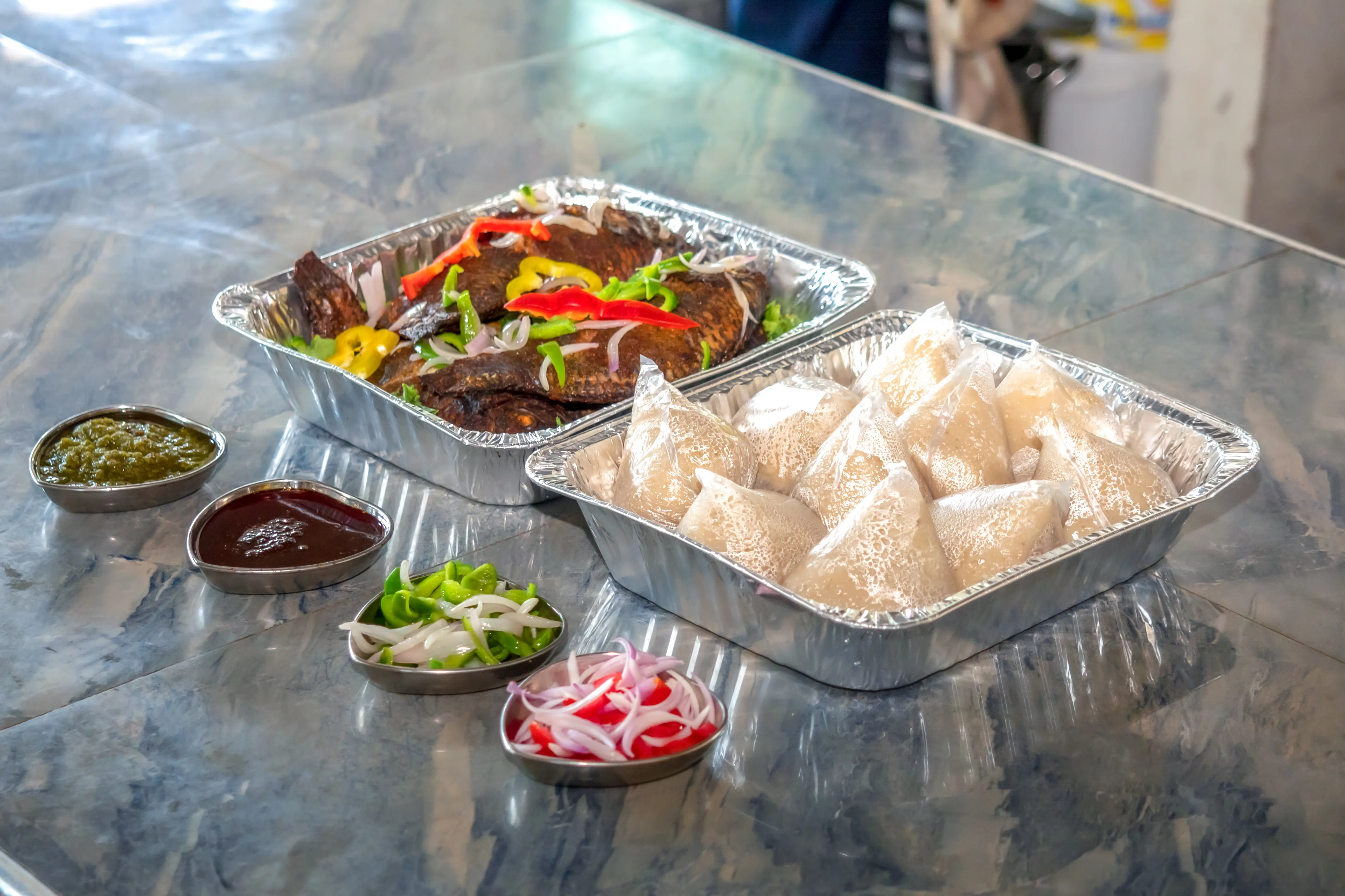 Large catering tray of fried fish with kenkey and banku — traditional Ghanaian cuisine